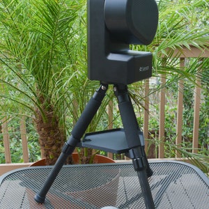 May include: A black camera with a tripod and a shelf on the tripod. The camera has a lens cover and a small logo that says "See360".