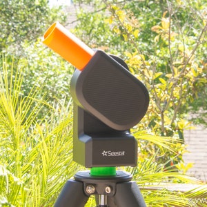 May include: A black telescope with an orange tube attached to a tripod. The telescope has a green base and the text "Seestar" printed on the side.