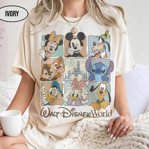 May include: An ivory t-shirt featuring a grid of nine squares displaying various Disney characters including Mickey Mouse, Minnie Mouse, Goofy, Donald Duck, Daisy Duck, Pluto, Chip, Dale, and Stitch, with the text Walt Disney World below.