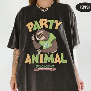 May include: Black t-shirt with a graphic of a sloth wearing sunglasses and a green shirt, with the words "PARTY ANIMAL" in yellow and green. Below the sloth is the word "ZOOTOPIA" in pink, with the phrase "BETTER ZOOGETHER" underneath.