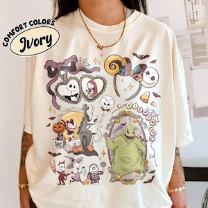 以下が含まれることがあります： アイボリー色のTシャツ。鮮やかなグラフィックは、「ナイトメアー・ビフォア・クリスマス」のキャラクターと要素が特徴です。デザインには、ジャック・スケリントン、サリー、ゼロ、ウギー・ブギー、その他の象徴的な画像が含まれています。「COMFORT COLORS」と「Ivory」の文字も表示されています。