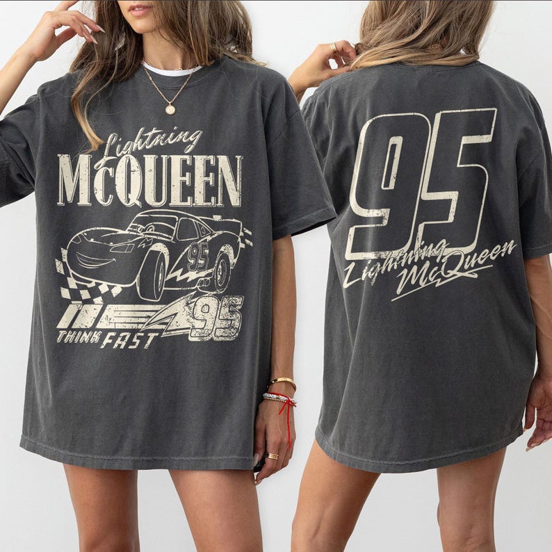 Puede incluir: Camiseta gris oscuro con Lightning McQueen de la pel&iacute;cula Cars. El gr&aacute;fico frontal incluye el personaje y el texto "Lightning McQueen", "95" y "Think Fast". La parte trasera muestra un gran "95" y el texto "Lightning McQueen".