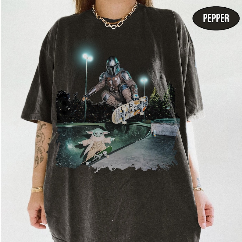 Pu&ograve; includere: Una t-shirt grigio antracite con una stampa grafica di un personaggio in armatura metallica che fa skateboard in una bowl, con una piccola creatura verde su uno skateboard sotto. Il testo PEPPER appare in un ovale nero in alto a destra.