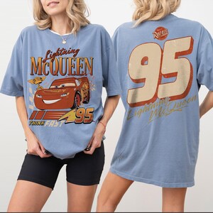 May include: Pale blue t-shirt featuring Lightning McQueen from the Cars film. The front graphic shows McQueen with the text "Lightning McQueen" and "95". The back of the shirt displays a large "95" and "Lightning McQueen" in a distressed style.