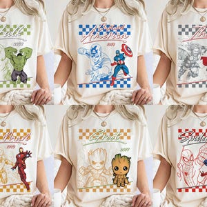 Puede incluir: Camisetas color crema con personajes de c&oacute;mics: Hulk, Capit&aacute;n Am&eacute;rica, Thor, Iron Man, Groot y Spider-Man. Cada camiseta muestra una ilustraci&oacute;n del personaje con su nombre y a&ntilde;o de origen, sobre un fondo a cuadros.