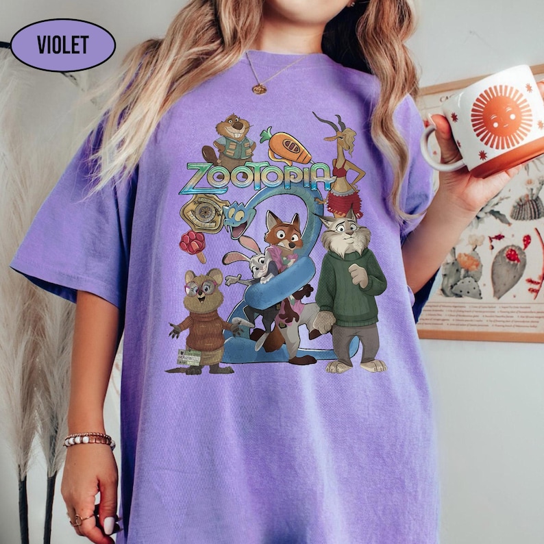 May include: A violet-colored t-shirt featuring a colorful graphic of characters from the animated film "Zootopia." The design includes the film's title and various animal characters. The shirt is a comfortable, oversized fit.