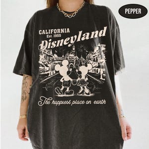 May include: Dark gray t-shirt with a Disneyland graphic. The design features Mickey and Minnie Mouse, the text "California Disneyland Est. 1955", and "The happiest place on earth". The shirt has a vintage, distressed look.