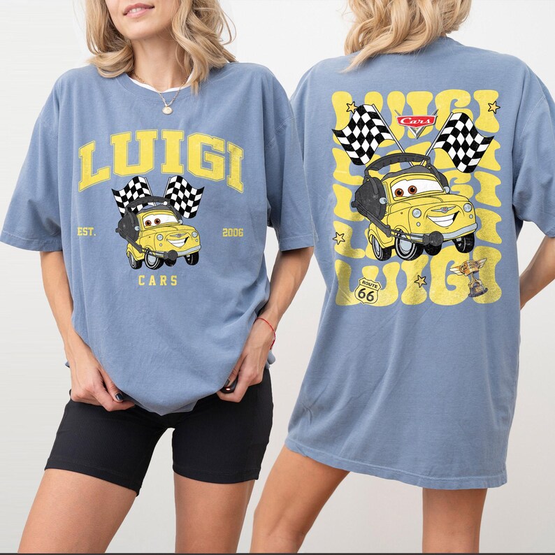 Peut inclure: T-shirt bleu clair avec un dessin de voiture de dessin anim&eacute; jaune, des drapeaux &agrave; damiers et le nom "Luigi". Le dos du t-shirt r&eacute;p&egrave;te le graphisme de la voiture et le nom "Luigi". Le t-shirt porte &eacute;galement le texte "EST. 2006" et "Route 66".