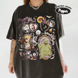 May include: Dark gray t-shirt featuring a colorful graphic design with characters and elements from "The Nightmare Before Christmas." The design includes Jack Skellington, Sally, and Oogie Boogie, along with bats, candy corn, and the words "Nightmare Before Christmas."