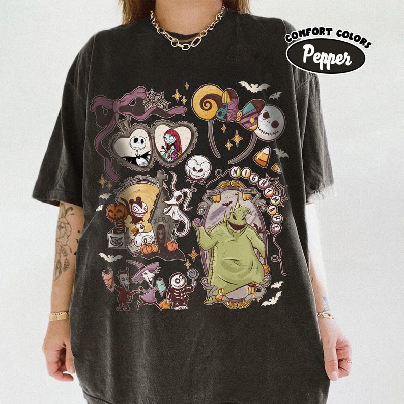 May include: Dark gray t-shirt featuring a colorful graphic design with characters and elements from "The Nightmare Before Christmas." The design includes Jack Skellington, Sally, and Oogie Boogie, along with bats, candy corn, and the words "Nightmare Before Christmas."