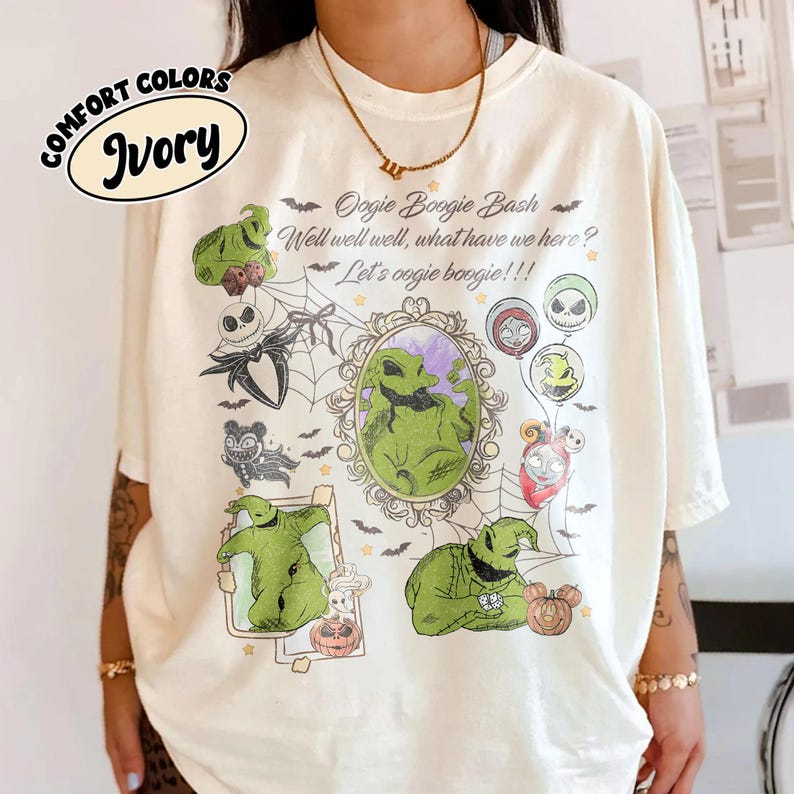 May include: Ivory-colored t-shirt featuring a graphic design with the text "Oogie Boogie Bash" and various characters. The design includes images of Oogie Boogie, Jack Skellington, and other characters from the movie. The shirt has a crew neck and short sleeves.