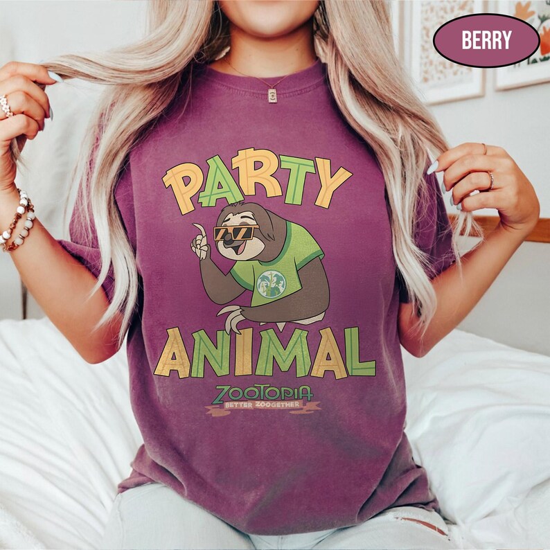 May include: Berry-colored t-shirt featuring a cartoon sloth wearing sunglasses and a green shirt, with the words "PARTY ANIMAL" in yellow and green. The shirt also has the text "ZOOTOPIA BETTER TOGETHER".