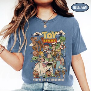 May include: Blue jean colored t-shirt featuring a graphic of characters from the animated movie Toy Story. The shirt has the words "Toy Story" and "You've Got a Friend in Me" printed on it. The shirt is a comfortable, casual style.