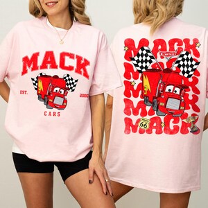 Peut inclure: T-shirt rose clair avec un dessin de camion rouge et le mot "MACK" en rouge. Le devant du t-shirt porte l'inscription "EST. 2006 CARS". Le dos du t-shirt porte le mot "MACK" r&eacute;p&eacute;t&eacute;.