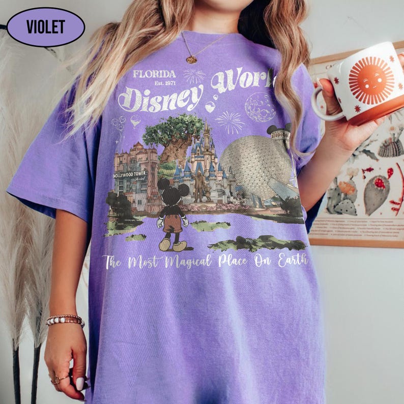 Puede incluir: Una camiseta violeta con un dise&ntilde;o de Disney World. El dise&ntilde;o incluye el texto "Florida Disney World Est. 1971" y una ilustraci&oacute;n de Mickey Mouse, un castillo y otros puntos de referencia del parque. Tambi&eacute;n se incluye el texto "The Most Magical Place On Earth".