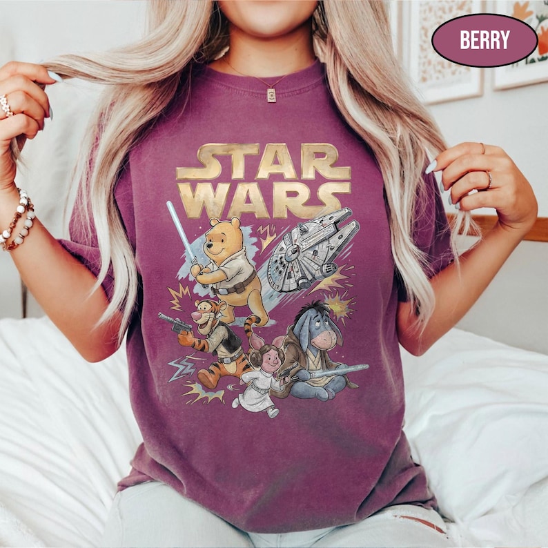 Puede incluir: Camiseta color bayas con el logo dorado "STAR WARS" y un gr&aacute;fico de los personajes de Winnie the Pooh como personajes de Star Wars. El dise&ntilde;o incluye un sable de luz, un Halc&oacute;n Milenario y otros elementos.