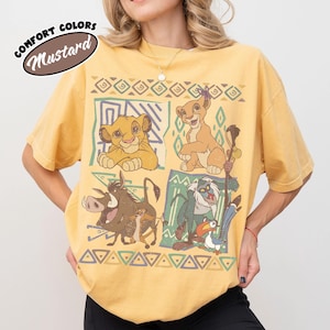 May include: A mustard yellow short-sleeve t-shirt featuring a graphic print of characters from The Lion King, including Simba, Nala, Pumbaa, Timon, Rafiki, and Zazu, arranged in four panels with geometric borders and the text Comfort Colors Mustard.