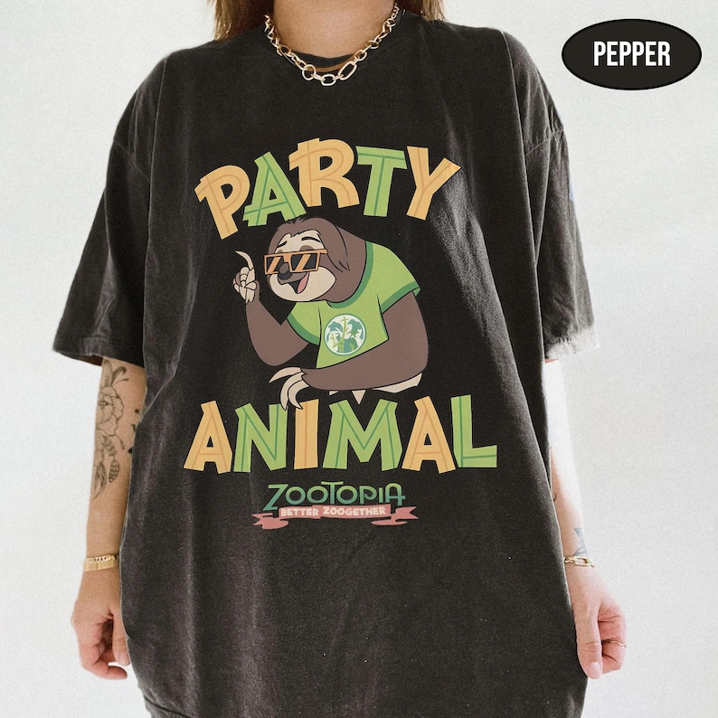 May include: Black t-shirt with a graphic of a sloth wearing sunglasses and a green shirt, with the words "PARTY ANIMAL" in yellow and green. Below the sloth is the word "ZOOTOPIA" in pink, with the phrase "BETTER ZOOGETHER" underneath.