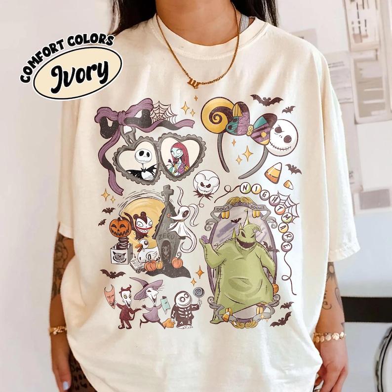 May include: Ivory-colored t-shirt with a colorful graphic featuring characters and elements from "The Nightmare Before Christmas." The design includes Jack Skellington, Sally, Zero, Oogie Boogie, and other iconic imagery. The text "COMFORT COLORS" and "Ivory" are also visible.