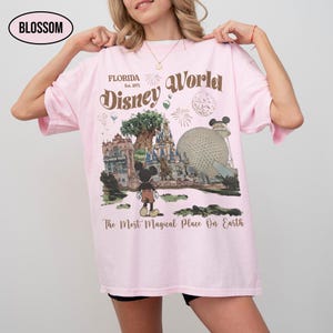 Puede incluir: Camiseta rosa claro con un gr&aacute;fico de Disney World. El dise&ntilde;o incluye el texto "Florida Est. 1971 Disney World" y una ilustraci&oacute;n de Mickey Mouse frente a los puntos de referencia del parque. Tambi&eacute;n se incluye el texto "The Most Magical Place On Earth".