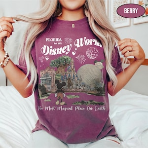 Puede incluir: Camiseta de color bayas con un dise&ntilde;o gr&aacute;fico de Disney World en Florida. El dise&ntilde;o incluye el texto "Florida Disney World Est. 1971" y una ilustraci&oacute;n de Mickey Mouse, el &Aacute;rbol de la Vida y Spaceship Earth. La camiseta tambi&eacute;n tiene la frase "The Most Magical Place On Earth."