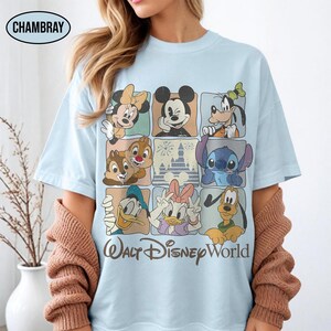 May include: A light blue t-shirt featuring a grid of Disney characters including Mickey Mouse, Minnie Mouse, Goofy, Chip, Dale, Stitch, Donald Duck, Daisy Duck, and Pluto, with a castle graphic and the text Walt Disney World below.