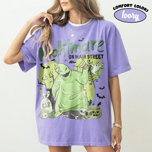 Puede incluir: Camiseta lila con un gr&aacute;fico que dice "Nightmare on Main Street". El dise&ntilde;o incluye un personaje verde, fantasmas, murci&eacute;lagos y una l&aacute;pida. La camiseta tiene mangas cortas y un corte holgado.