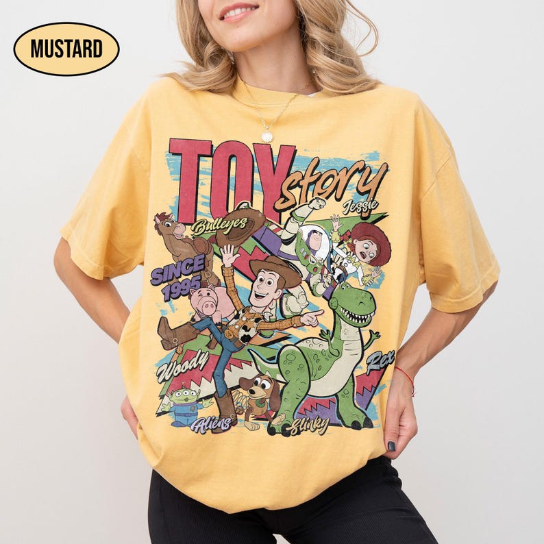 Puede incluir: Camiseta de color mostaza con un gr&aacute;fico de personajes de la pel&iacute;cula de animaci&oacute;n "Toy Story". El dise&ntilde;o incluye a Woody, Buzz Lightyear, Jessie, Rex y otros personajes, con el texto "TOY STORY" y "SINCE 1995".