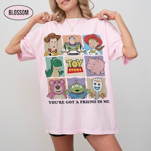 May include: Light pink t-shirt featuring a colorful graphic of Toy Story characters. The design includes Woody, Buzz Lightyear, Jessie, Rex, Hamm, Lotso, the Aliens, and Forky. The text "TOY STORY" and "YOU'RE GOT A FRIEND IN ME" are also displayed.