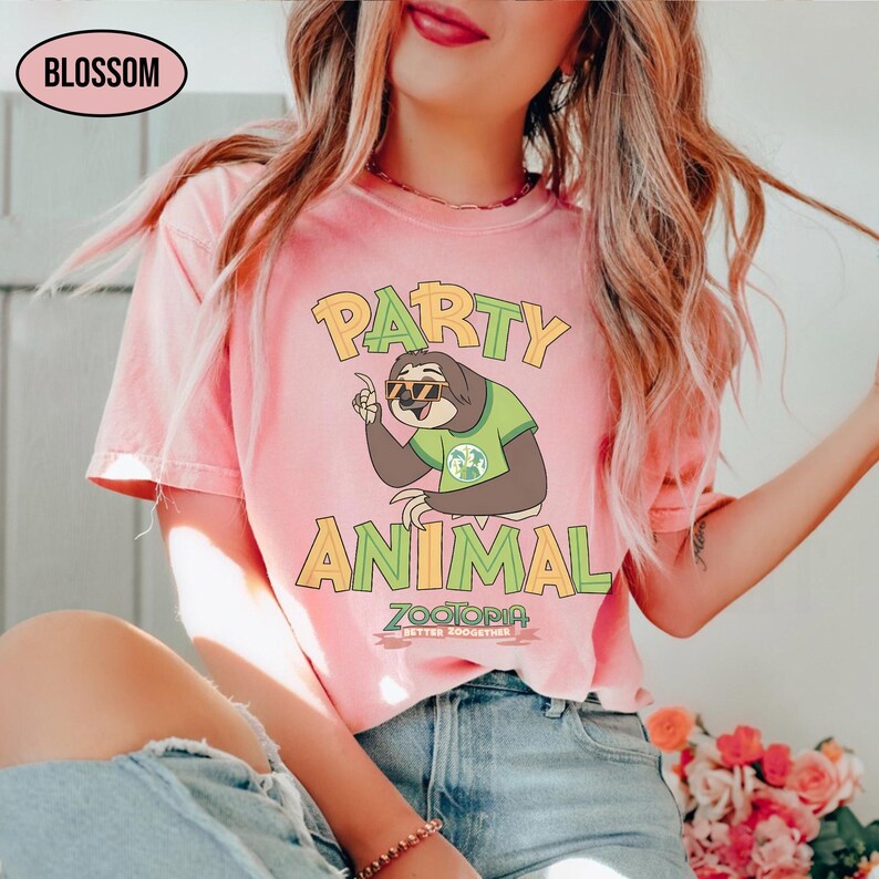 May include: A light pink t-shirt with the words "PARTY ANIMAL" in yellow and green. A cartoon sloth wearing sunglasses and a green shirt is in the center. The word "ZOOTOPIA" is below the sloth, with the text "BETTER TOGETHER".