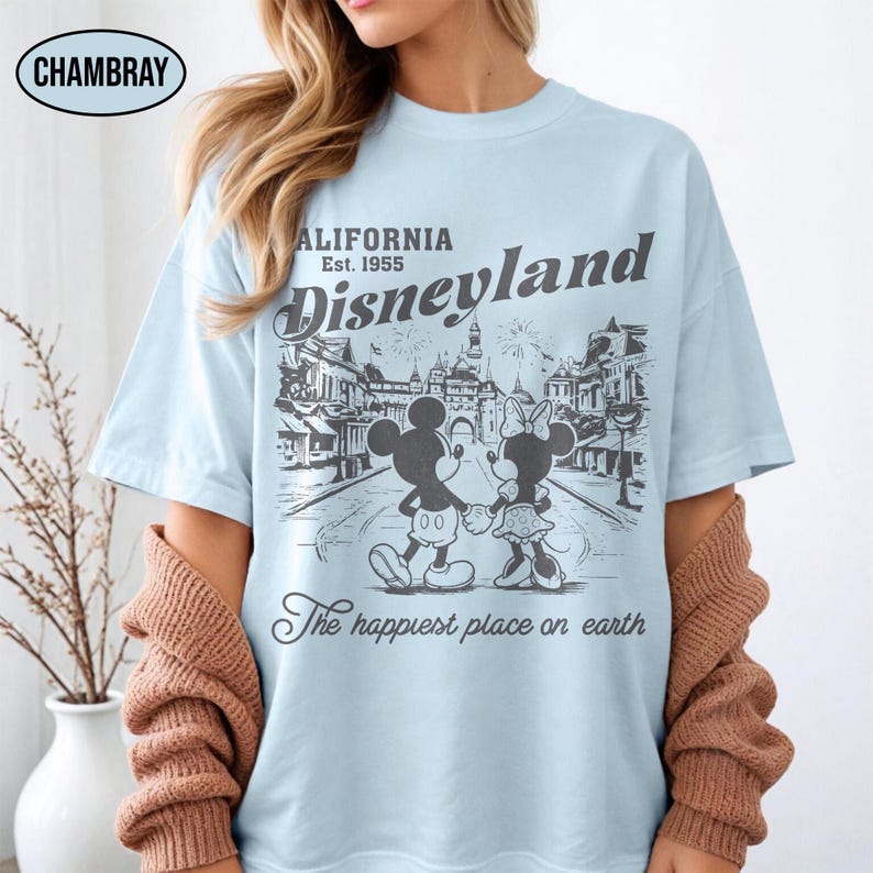 May include: Light blue t-shirt featuring a black and white graphic of Mickey and Minnie Mouse holding hands in front of a Disneyland scene. The shirt includes the text "California Disneyland Est. 1955" and "The happiest place on earth."