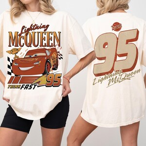 May include: Cream-coloured t-shirt featuring Lightning McQueen from the Cars film. The front graphic includes the character's image, the text "Lightning McQueen," and the number "95." The back displays a large "95" and "Lightning McQueen" text.