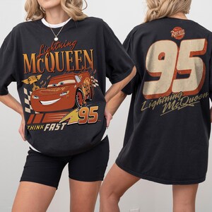 May include: Black t-shirt featuring Lightning McQueen from the movie Cars. The front graphic shows McQueen with the text "Lightning McQueen", "95", and "Think Fast". The back of the shirt displays "95" and "Lightning McQueen".