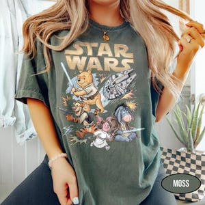 Puede incluir: Camiseta verde musgo con un gr&aacute;fico de Star Wars con personajes de Winnie the Pooh. El dise&ntilde;o incluye a Pooh con un sable de luz, Tigger con un blaster, Piglet, Eeyore y el Halc&oacute;n Milenario. El texto "STAR WARS" es dorado.