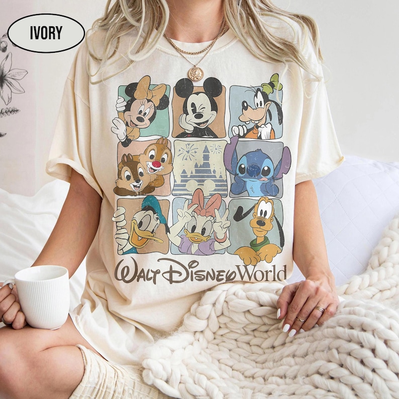 May include: An ivory t-shirt featuring a grid of nine squares displaying various Disney characters including Mickey Mouse, Minnie Mouse, Goofy, Donald Duck, Daisy Duck, Pluto, Chip, Dale, and Stitch, with the text Walt Disney World below.