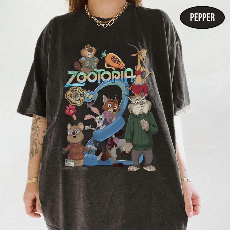 May include: Dark gray t-shirt featuring a colorful graphic of characters from the animated movie Zootopia. The design includes the word "Zootopia" in a vibrant font, along with the number "2". The shirt has a vintage, worn look.