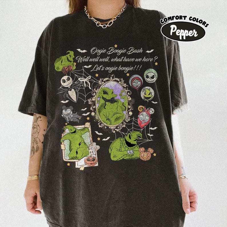 May include: Dark gray t-shirt featuring a graphic design with the text "Oogie Boogie Bash" and various characters. The design includes images of Oogie Boogie, Jack Skellington, and other characters from the movie. The shirt is labeled "Comfort Colors Pepper".
