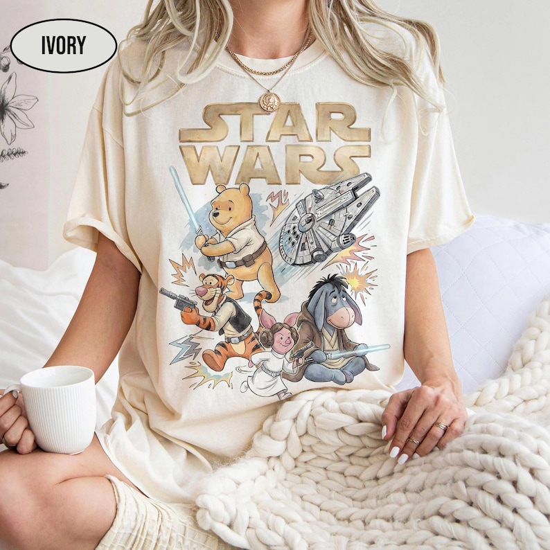 Puede incluir: Camiseta de color marfil con un dise&ntilde;o de Star Wars con personajes de Winnie the Pooh. El dise&ntilde;o incluye a Pooh con un sable de luz, Tigger con un blaster y Eeyore. El logotipo de Star Wars est&aacute; en la parte superior.