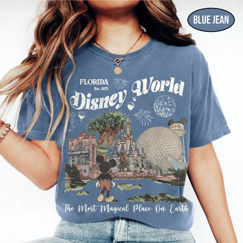 Puede incluir: Camiseta azul vaquero con un dise&ntilde;o gr&aacute;fico de Disney World en Florida. El dise&ntilde;o incluye el texto "Florida Disney World Est. 1971" y "The Most Magical Place On Earth". La camiseta presenta im&aacute;genes de la Hollywood Tower, el castillo de Cenicienta y Spaceship Earth.