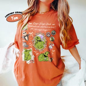 May include: A yam-colored Comfort Colors t-shirt featuring a graphic design with the text "Oogie Boogie Bash" and various characters. The design includes a green character in a frame and other Halloween-themed elements.