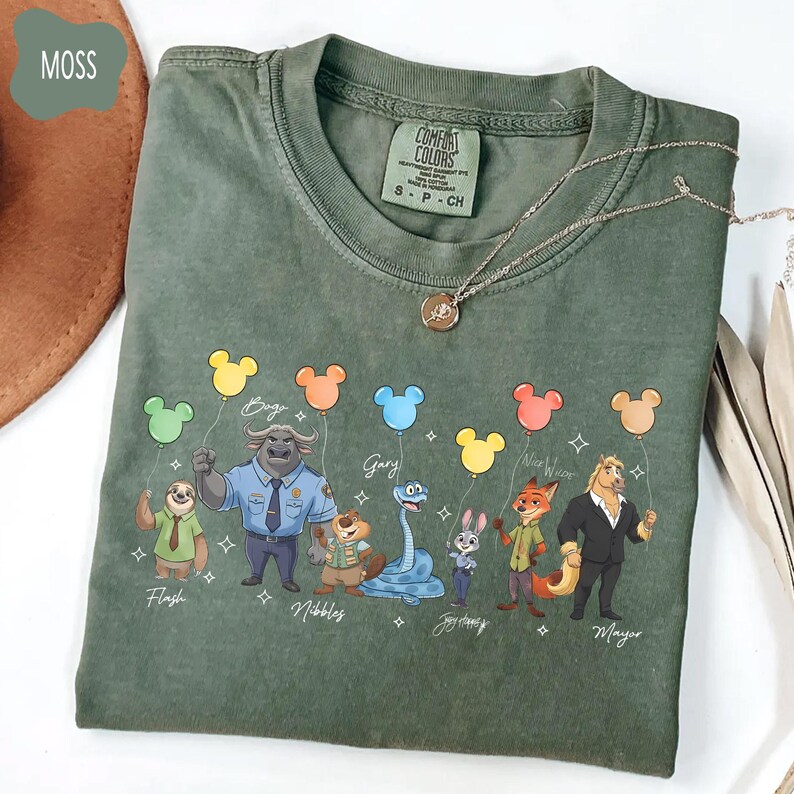 Puede incluir: Una camiseta verde musgo con personajes de una popular pel&iacute;cula animada sosteniendo globos con forma de Mickey Mouse. Los personajes incluyen a Flash, Bogo, Gary, Nibbles, Judy Hopps, Nick Wilde y el alcalde. Tambi&eacute;n se ve un collar plateado con un colgante.