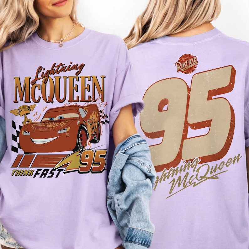 May include: A lilac t-shirt with a graphic of Lightning McQueen from the Cars film. The front displays "Lightning McQueen", "Think Fast", a cartoon car image, and the number "95". The back features a large "95" and "Lightning McQueen" text in a vintage style.