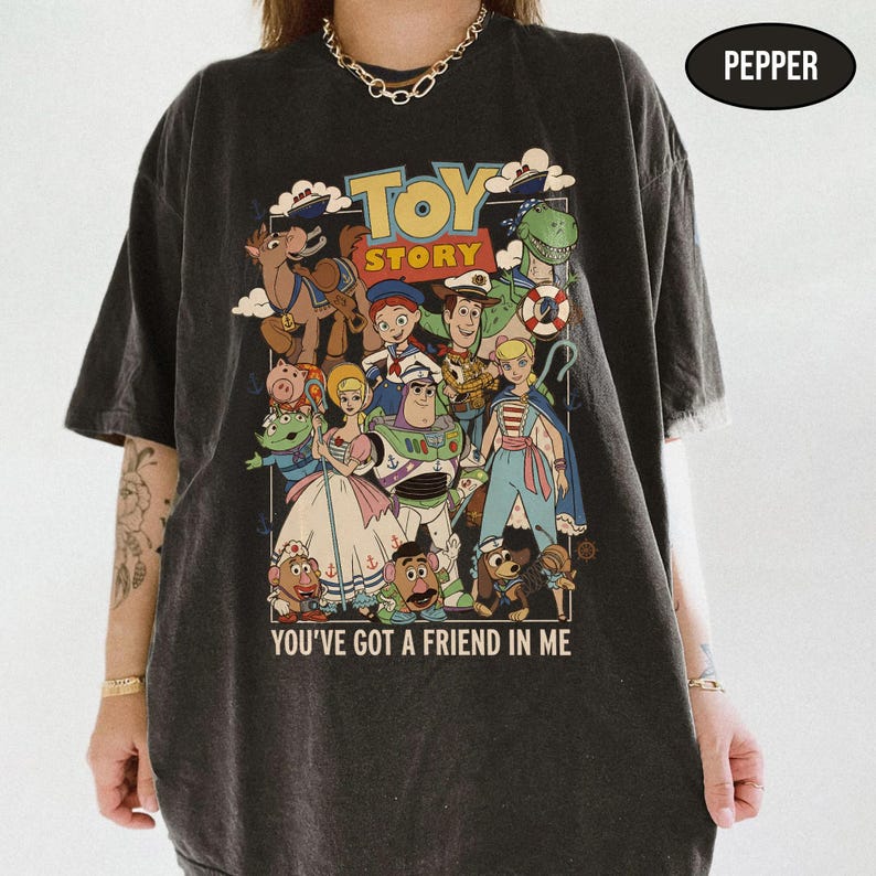 May include: Dark gray t-shirt featuring a colorful graphic of characters from the animated film "Toy Story." The design includes the film's title and the phrase "You've Got a Friend in Me."