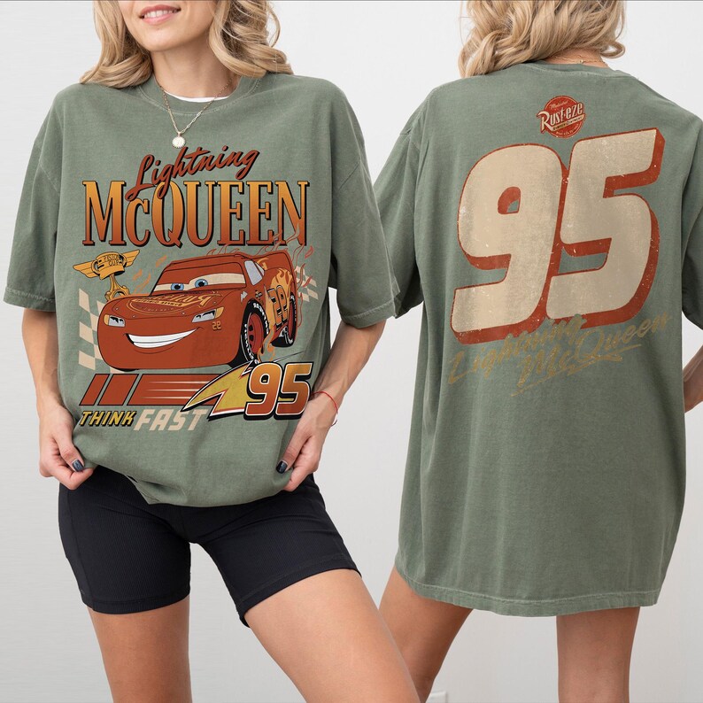 May include: Olive green t-shirt featuring Lightning McQueen from the Cars movie. The front graphic includes the character's image, the text "Lightning McQueen", and "95". The back of the shirt displays a large "95" and the text "Lightning McQueen".