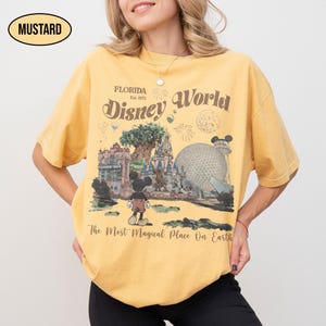 Puede incluir: Camiseta de color mostaza con un gr&aacute;fico de Disney World. El dise&ntilde;o incluye a Mickey Mouse, el nombre del parque de Florida y la frase "The Most Magical Place On Earth". La camiseta tiene un aspecto vintage y ligeramente descolorido.