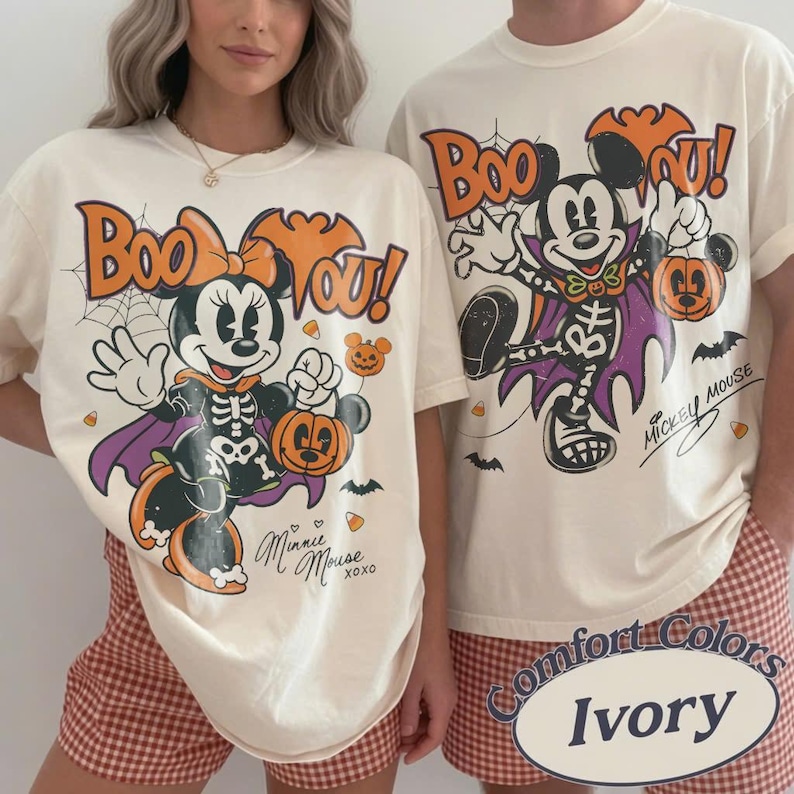 May include: Two ivory t-shirts featuring Halloween-themed graphics. One shirt displays Minnie Mouse in a skeleton costume with a pumpkin and the text "Boo You!" and "Minnie Mouse". The other shirt shows Mickey Mouse in a skeleton costume with a pumpkin and the text "Boo You!" and "Mickey Mouse".