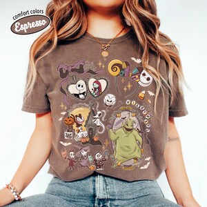 May include: A brown t-shirt with a graphic featuring characters from "The Nightmare Before Christmas." The design includes Jack Skellington, Sally, Zero, and Oogie Boogie. The shirt has the words "comfort colors" and "Espresso" in a circle.