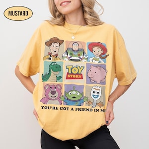 May include: Mustard-colored t-shirt featuring a grid of Toy Story characters, including Woody, Buzz Lightyear, and others. The shirt has the text "TOY STORY" and "YOU'RE GOT A FRIEND IN ME".