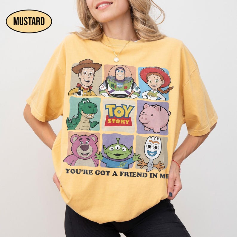 May include: Mustard-colored t-shirt featuring a grid of Toy Story characters, including Woody, Buzz Lightyear, and others. The shirt has the text "TOY STORY" and "YOU'RE GOT A FRIEND IN ME".