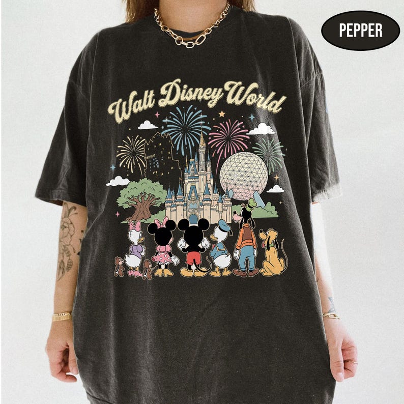 May include: Dark grey t-shirt with a colourful graphic of Disney characters and fireworks in front of a castle and a large sphere. The words "Walt Disney World" are arched across the top of the design.